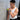 Person leaning against a wall with a massage ball, wearing a white sleeveless shirt and black pants.